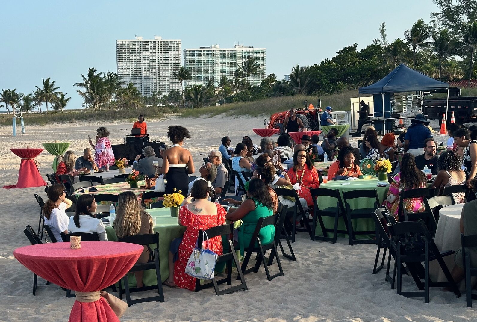 Image of a reception on the beach with elegantly dressed attendees and colorful tables