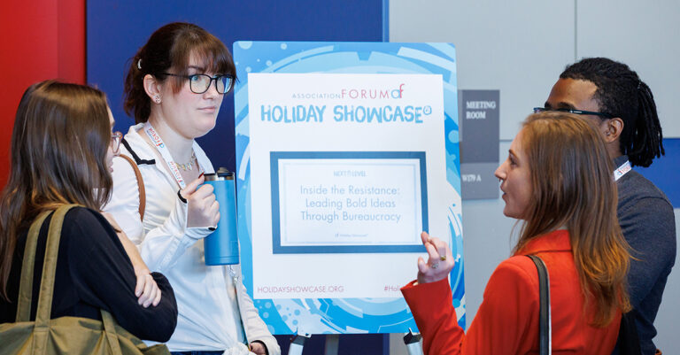 A group of engaged participants chat in front of a session sign for Holiday Showcase 2025